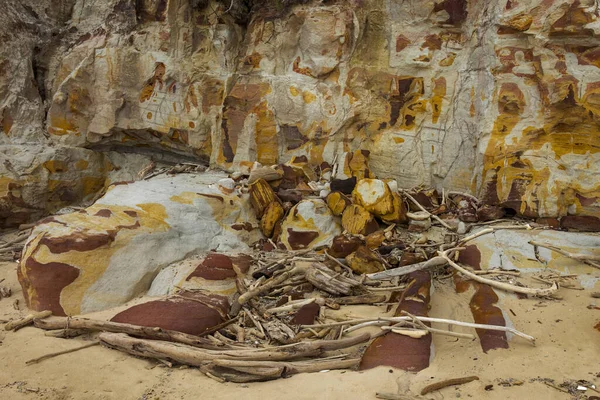 Colorful Sandstone and Sand at the Beach with Driftwood Piled Up
