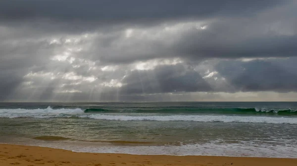 Sun rays breaking through clouds forming streaks of sunlight at Wamberal Beach