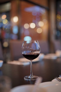 Düşük açı, kırmızı şarap ve ince saplı kristal berrak şarap kadehinin perspektifini kapatın. Restoranın arka planında bulanık bir sahne ve dikey ışık festivali olsun..                 