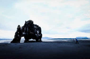 Hvitserkur manzarası, keskin fil şekli ya da dinozor aganst siyah kum ve gri gökyüzü, fotoğrafçıyla fotoğraf çeken küçük mavi gökyüzü. İzlanda dönüm noktası kaderi.