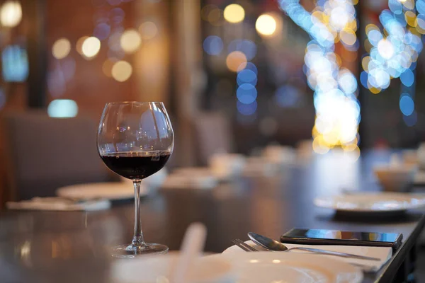 stock image                                Low angle close up perspective of crystal clear wine glass filled with red wine and slim stem on the table with blurry restaurant background scene and bokeh light festival. Alone celebration.