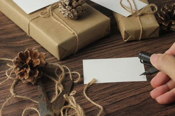 男性の手は新しい年の贈り物や書き込みカードを包む茶色の木製のテーブルに — ストック写真