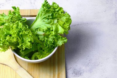 Marul beyaz bir kaseye ve beyaz bir masanın üzerindeki kesme tahtasına konmuş. Sebze salatası. Vejetaryen yemeği. Temiz yemek. Yeşil sebze.