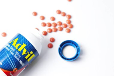 Washington, ABD - 02 Ekim 2022: Advil şişeleri ve haplar beyaz bir masaya yayıldı. Ateş, ağrı kesici, popüler Amerikan ağrı kesici, ibuprofen..