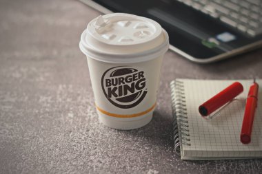 Washington, USA - January 18 2023 : Coffee Cup Mug Burger King with notebook and laptop on gray table In studio lighting, Burger King is a popular food in America.