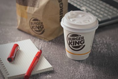 Washington, USA - January 18 2023 : Coffee Cup Mug Burger King with notebook and laptop on gray table In studio lighting, Burger King is a popular food in America.