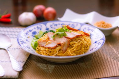 Çin usulü tabak şeklinde ızgara domuz etli yumurta eriştesi. Tahta masa üzerinde çay ve çay.