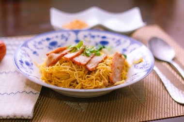 Çin usulü tabak şeklinde ızgara domuz etli yumurta eriştesi. Tahta masa üzerinde çay ve çay.