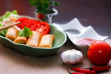 Kızarmış börekler, sebzeler ve domatesler yeşil yaprak şeklinde bir tabağa konmuş siyah ahşap bir masa ve Tayland sosu..