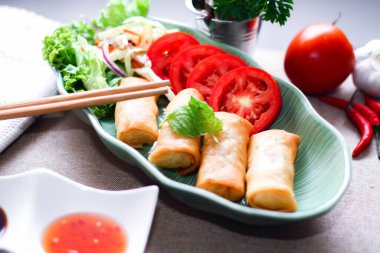 Kızarmış börekler, sebzeler ve domatesler yeşil yaprak şeklinde bir tabağa konmuş siyah ahşap bir masa ve Tayland sosu..