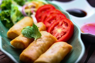 Kızarmış börekler, sebzeler ve domatesler yeşil yaprak şeklinde bir tabağa konmuş siyah ahşap bir masa ve Tayland sosu..