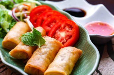 Kızarmış börekler, sebzeler ve domatesler yeşil yaprak şeklinde bir tabağa konmuş siyah ahşap bir masa ve Tayland sosu..