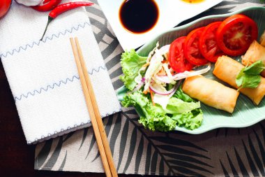 Kızarmış börekler, sebzeler ve domatesler yeşil yaprak şeklinde bir tabağa konmuş siyah ahşap bir masa ve Tayland sosu..