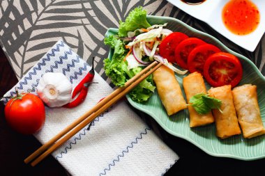 Kızarmış börekler, sebzeler ve domatesler yeşil yaprak şeklinde bir tabağa konmuş siyah ahşap bir masa ve Tayland sosu..