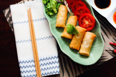Kızarmış börekler, sebzeler ve domatesler yeşil yaprak şeklinde bir tabağa konmuş siyah ahşap bir masa ve Tayland sosu..