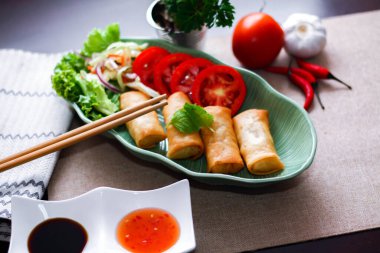 Kızarmış börekler, sebzeler ve domatesler yeşil yaprak şeklinde bir tabağa konmuş siyah ahşap bir masa ve Tayland sosu..