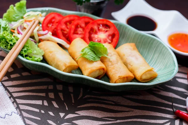 stock image Fried spring rolls, vegetables and tomatoes placed in a green leaf shape plate on a black wooden table and dipping sauce in thailand.