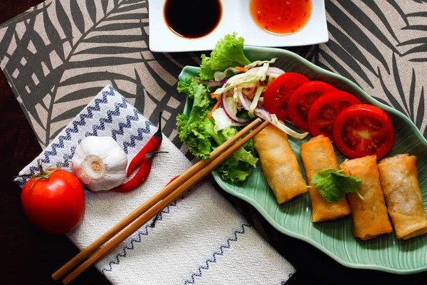 stock image Fried spring rolls, vegetables and tomatoes placed in a green leaf shape plate on a black wooden table and dipping sauce in thailand.