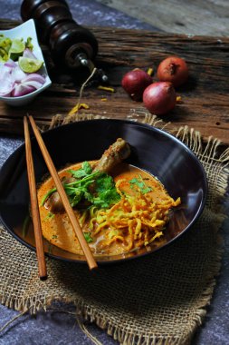 Khao Soi Kai, Kuzey Tayland yemeği ahşap bir masada soğan ve sebzelerle siyah bir kasede servis edilir..