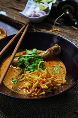 Khao Soi Kai, Kuzey Tayland yemeği ahşap bir masada soğan ve sebzelerle siyah bir kasede servis edilir..