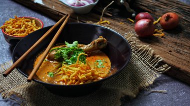 Khao Soi Kai, Kuzey Tayland yemeği ahşap bir masada soğan ve sebzelerle siyah bir kasede servis edilir..