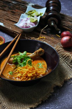 Khao Soi Kai, Kuzey Tayland yemeği ahşap bir masada soğan ve sebzelerle siyah bir kasede servis edilir..