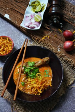 Khao Soi Kai, Kuzey Tayland yemeği ahşap bir masada soğan ve sebzelerle siyah bir kasede servis edilir..