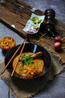 Khao Soi Kai, Kuzey Tayland yemeği ahşap bir masada soğan ve sebzelerle siyah bir kasede servis edilir..