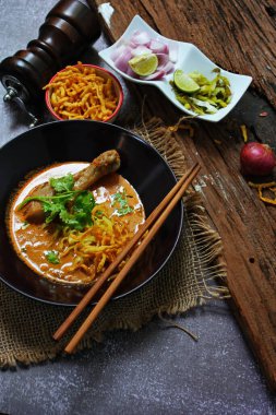 Khao Soi Kai, Kuzey Tayland yemeği ahşap bir masada soğan ve sebzelerle siyah bir kasede servis edilir..