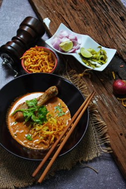 Khao Soi Kai, Kuzey Tayland yemeği ahşap bir masada soğan ve sebzelerle siyah bir kasede servis edilir..