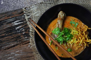 Khao Soi Kai, Kuzey Tayland yemeği ahşap bir masada soğan ve sebzelerle siyah bir kasede servis edilir..