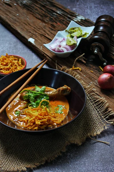 カオソイカイ 北タイ料理木製のテーブルの上にエシャロットと野菜と黒のボウルで提供しています — ストック写真
