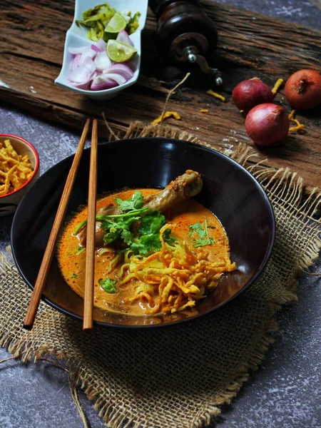 Khao Soi Kai, Kuzey Tayland yemeği ahşap bir masada soğan ve sebzelerle siyah bir kasede servis edilir..