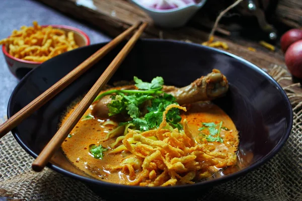 Khao Soi Kai, Kuzey Tayland yemeği ahşap bir masada soğan ve sebzelerle siyah bir kasede servis edilir..