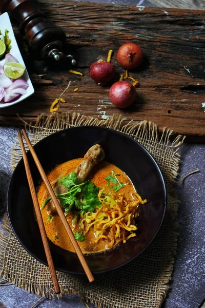 Khao Soi Kai, Kuzey Tayland yemeği ahşap bir masada soğan ve sebzelerle siyah bir kasede servis edilir..