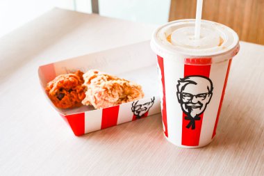 Bangkok, Tayland - 07 Ocak 2024 - Kağıt tabakta iki parça KFC kızarmış tavuk ve bir KFC restoranının içindeki masada üzerinde KFC logosu olan bir meşrubat bardağı.