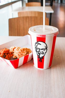 Bangkok, Tayland - 07 Ocak 2024 - Kağıt tabakta iki parça KFC kızarmış tavuk ve bir KFC restoranının içindeki masada üzerinde KFC logosu olan bir meşrubat bardağı.