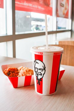 Bangkok, Tayland - 07 Ocak 2024 - Kağıt tabakta iki parça KFC kızarmış tavuk ve bir KFC restoranının içindeki masada üzerinde KFC logosu olan bir meşrubat bardağı.