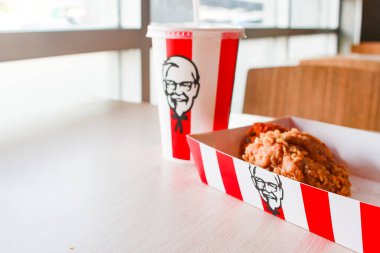 Bangkok, Tayland - 07 Ocak 2024 - Kağıt tabakta iki parça KFC kızarmış tavuk ve bir KFC restoranının içindeki masada üzerinde KFC logosu olan bir meşrubat bardağı.