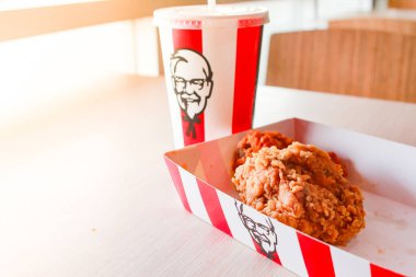 Bangkok, Tayland - 07 Ocak 2024 - Kağıt tabakta iki parça KFC kızarmış tavuk ve bir KFC restoranının içindeki masada üzerinde KFC logosu olan bir meşrubat bardağı.