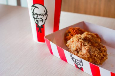 Bangkok, Tayland - 07 Ocak 2024 - Kağıt tabakta iki parça KFC kızarmış tavuk ve bir KFC restoranının içindeki masada üzerinde KFC logosu olan bir meşrubat bardağı.