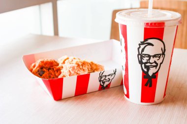Bangkok, Tayland - 07 Ocak 2024 - Kağıt tabakta iki parça KFC kızarmış tavuk ve bir KFC restoranının içindeki masada üzerinde KFC logosu olan bir meşrubat bardağı.