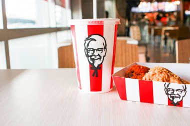 Bangkok, Tayland - 07 Ocak 2024 - Kağıt tabakta iki parça KFC kızarmış tavuk ve bir KFC restoranının içindeki masada üzerinde KFC logosu olan bir meşrubat bardağı.
