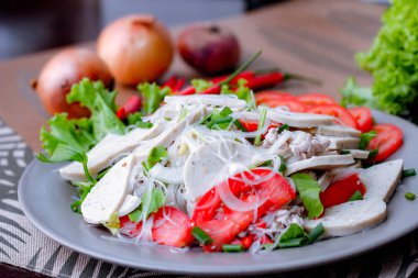 Gri bir tabakta servis edilen Vietnam sosisli Baharatlı Cam Erişte Salatası Ahşap masa ve çeşitli sebzeler.