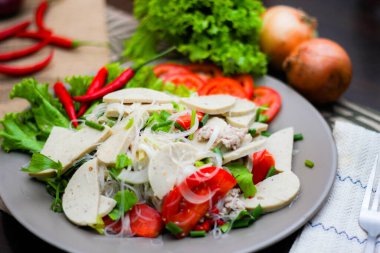 Gri bir tabakta servis edilen Vietnam sosisli Baharatlı Cam Erişte Salatası Ahşap masa ve çeşitli sebzeler.