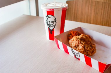 Bangkok, Tayland - 07 Ocak 2024 - Kağıt tabakta iki parça KFC kızarmış tavuk ve bir KFC restoranının içindeki masada üzerinde KFC logosu olan bir meşrubat bardağı.