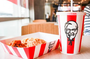 Bangkok, Tayland - 07 Ocak 2024 - Kağıt tabakta iki parça KFC kızarmış tavuk ve bir KFC restoranının içindeki masada üzerinde KFC logosu olan bir meşrubat bardağı.