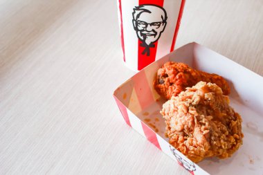 Bangkok, Tayland - 07 Ocak 2024 - Kağıt tabakta iki parça KFC kızarmış tavuk ve bir KFC restoranının içindeki masada üzerinde KFC logosu olan bir meşrubat bardağı.