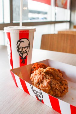 Bangkok, Tayland - 07 Ocak 2024 - Kağıt tabakta iki parça KFC kızarmış tavuk ve bir KFC restoranının içindeki masada üzerinde KFC logosu olan bir meşrubat bardağı.