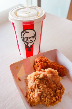 Bangkok, Tayland - 07 Ocak 2024 - Kağıt tabakta iki parça KFC kızarmış tavuk ve bir KFC restoranının içindeki masada üzerinde KFC logosu olan bir meşrubat bardağı.